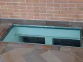 Bocche di lupo moderne in vetro, incastonate in un pavimento di piastrelle color terra, illuminano uno spazio sottostante.