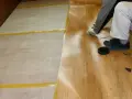 Układanie linoleum na beton: pracownik w rękawiczkach przycina wykładzinę, przygotowując ją do położenia.