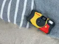 Aparat jednorazowy firmy Kodak leży na plaży obok ręcznika. Idealny do uchwycenia letnich wspomnień.