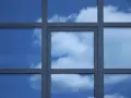 Szpros dzieli okno na kwadratowe pola, w których odbija się błękitne niebo z chmurami.