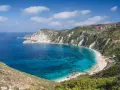 Malownicza zatoka z turkusową wodą i piaszczystą plażą, otoczona stromymi, zielonymi klifami. To idealne miejsce na wypoczynek na wyspie na Morzu Jońskim.