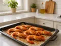 Gambones al horno listos para servir, con un toque de especias y aceite de oliva, sobre una bandeja en una cocina luminosa.