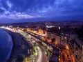 Night view of the Promenade des Anglais from Castle Hill, Nice, France, with city lights twinkling and car trails on the road.