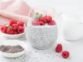 Pyszny deser z chia z mlekiem, ozdobiony malinami i miętą. Obok miseczki z nasionami chia i dzbanuszek z mlekiem.