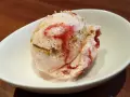 Ein Löffel cremiges strawberry cheesecake eis mit Erdbeersauce und Keksstückchen in einer weißen Schale.