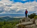 Turysta z plecakiem podziwia rozległą panoramę Gór Opawskich. Chmury na niebie tworzą dramatyczny spektakl.