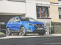 Błękitny Nissan Qashqai 2018 zaparkowany przed nowoczesnym budynkiem z garażem.
