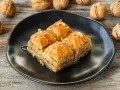 Słodka baklawa na czarnym talerzu, idealna do domowego przepisu. Orzechy włoskie w tle.