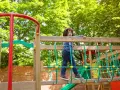 Chłopiec na placu zabaw, wesoły park rysunek. Dziecko wspina się po drewnianej konstrukcji z zielonymi linami.