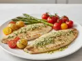 Dos filetes de merluza a la plancha con hierbas, acompañados de patatas pequeñas, tomates cherry y espárragos.