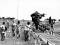 Sul set di un film, un operatore manovra una cinepresa su binari per un piano sequenza. Altri membri della troupe osservano e lavorano.
