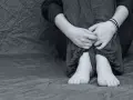 Dziecko w spodniach w paski, skulone, z rękami na kolanach. Czasem bunt 10 latki objawia się ciszą i smutkiem.