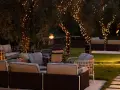 Accogliente terrazzo con divani e poltrone, illuminato da lucine sugli alberi e faretti. Perfetto per serate magiche.