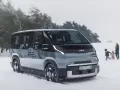 Szary elektryczny minivan Kia EV9 na śniegu, z rodziną w tle.