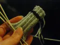 En hand håller stickor och ett ljusgrönt stickat tyg med en mörk rand. Det ser ut som att någon ska sticka avig maska.