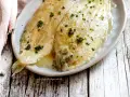 Sogliola alla mugnaia dorata e succulenta, cosparsa di prezzemolo fresco, servita su un piatto ovale.