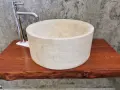 Lavabo cilindrico in pietra naturale chiara, con rubinetto cromato, su un piano in legno grezzo. Un esempio di come i nomi delle pietre naturali si trasformano in design unici.