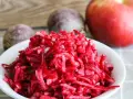 Frischer Salat aus rote Bete raspeln, mit einem Apfel und ganzen Rote Beten im Hintergrund.