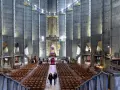 Intérieur de la cathédrale de Royan, avec ses murs en béton brut, ses rangées de chaises et son vitrail coloré au fond.