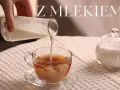 Ręka wlewa mleko do szklanki z herbatą, tworząc piękne smugi. Obok stoi cukiernica. Idealna herbata z mlekiem na chłodny dzień.