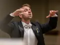Dyrygent w garniturze z kokardką, prowadzący wykonanie Carmina Burana, z ukraińską wstążką na klapie.