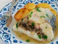 Deliciosa merluza con gambas y champiñones, servida con patatas doradas en un plato azul y blanco.
