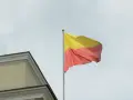 Flaga Łotwy z żółtym i czerwonym pasem, powiewająca na maszcie obok budynku.