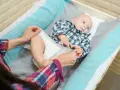 Mama sprawdza, kiedy zmienić rozmiar pieluchy maluszkowi. Dziecko leży na przewijaku w kratkę.