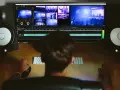 Osoba edytuje wideo na komputerze, otoczona przez jakie monitory studyjne. Widok zza pleców na ekran z wieloma kadrami i linią czasu.