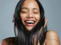 Une femme rit aux éclats, ses yeux fermés. Ses cheveux noirs encadrent son visage radieux, témoignant de la beauté que la vitamine B7 peut apporter.