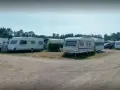 Ställplatser med husvagnar och bilar på Olles camping. Träd och blå himmel syns i bakgrunden.