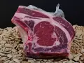 A vacuum-sealed raw beef steak with marbling sits on a bed of wood chips and small nuts.