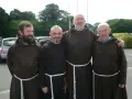 Four monk priests in brown robes stand together outdoors.