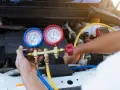 A mechanic uses a manifold gauge set to check for a freon leak in a car's AC system.