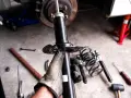 Mano guantata tiene un ammortizzatore nuovo, pronto per sostituire quelli scarichi dell'auto. Attrezzi e molle a vista.