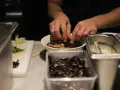 Hände garnieren eine Schüssel mit Ramen-Nudeln in Berlin. Daneben liegen Zutaten bereit.