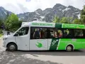 Elektryczny bus na Morskie Oko, z pasażerami w środku, na tle gór.