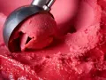 Ein Löffel nimmt eine Kugel leuchtend rotes Eis auf. Es sieht aus wie ein köstliches Blaubeereis, das zum Genießen bereit ist.