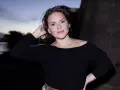 Emiliana Torrini, la chanteuse, pose au crépuscule près de l'eau, une main dans ses cheveux.
