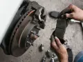 Mechanik pokazuje zużyte klocki hamulcowe przed ich wymianą. Sprawdź wymiana klocków hamulcowych cena.