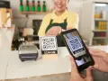 Cliente usa su móvil para escanear un código QR y hacer su carta digital. Un datáfono y otro código QR esperan en el mostrador.