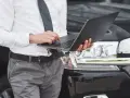 Mężczyzna w koszuli i krawacie korzysta z laptopa, przygotowując się do przerejestrowania samochodu.