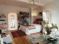 Ideas para decorar habitación estudio: cama blanca, espejo ondulado, estanterías con libros y arte, alfombras coloridas y un sofá acogedor.