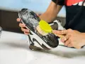 Mani che puliscono la suola di una scarpa con una spazzola gialla e schiuma. Un modo efficace per capire come pulire la suola delle scarpe.