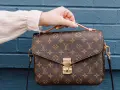 Una mano tiene una borsa Louis Vuitton con il classico monogramma. Un'icona di stile, che ci ricorda dove louis vuitton nasce: dalla maestria artigianale francese.