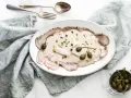 Eleganckie vitello tonnato z kremowym sosem, kaparami i natką pietruszki na białym talerzu, obok srebrnych sztućców i lnianej serwetki.