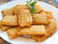 Pencas rellenas doradas y crujientes, apiladas en un plato blanco, con una ramita de perejil fresco.