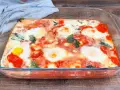 Uova alla contadina appena sfornate in teglia di vetro, con pomodoro e basilico.
