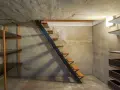 Escaliers métalliques menant à une cave en cours d'aménagement, avec étagères brutes et murs en béton. Idéal pour creuser une cave sous sa maison.