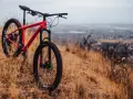 A red hardtail bike meaning adventure, rests on a dry, grassy hillside overlooking a hazy city.